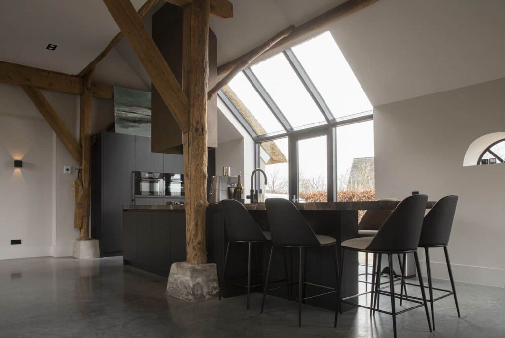 Gevlinderde betonvloer in de keuken in Ochten. De keuken is zwart met een marmeren blad. Aan het kookeiland staat zwarte barkrukken.