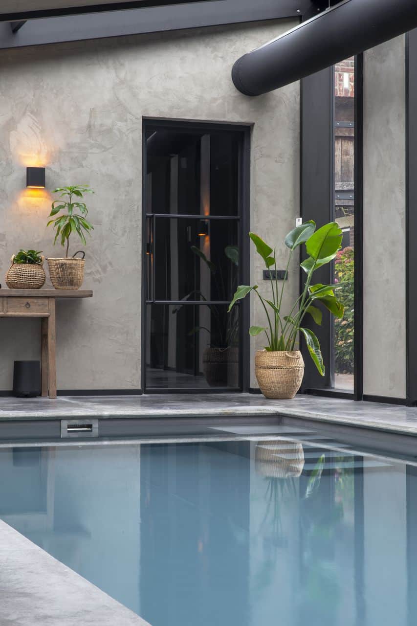 Gevlinderde betonvloer met American Clay kleiwanden en stalen deur rondom een zwembad in een poolhouse in Cuijk.