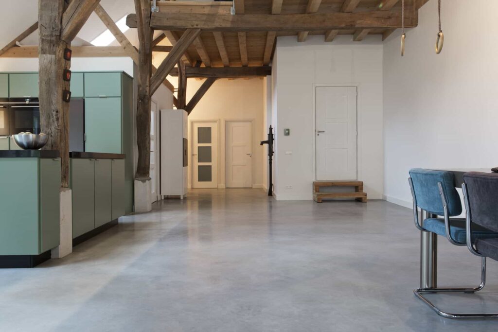 Woonboerderij in Rijswijk met een gevlinderde betonvloer van Willem Designvloeren gecombineerd met een turquoise keuken en gekleurde eetkamer stoelen.