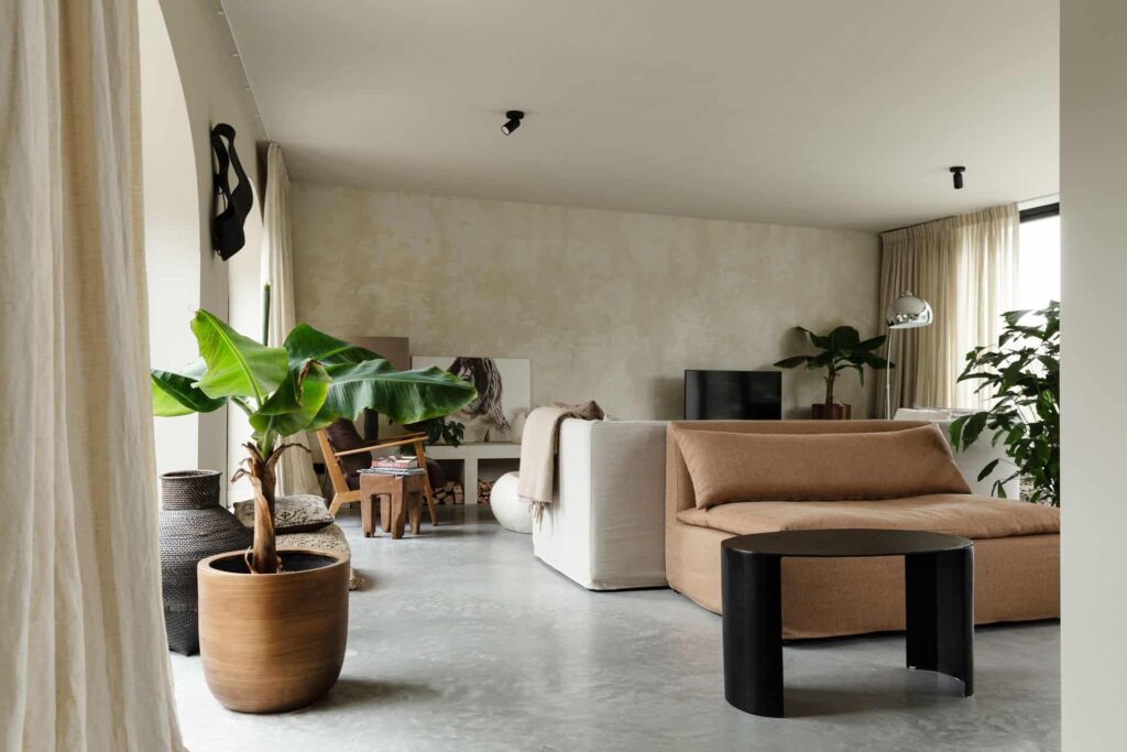 Woonkamer in Rijnsburg. Hierin ligt een gevlinderde betonvloer en dit is gecombineerd met veel houten en beige details.