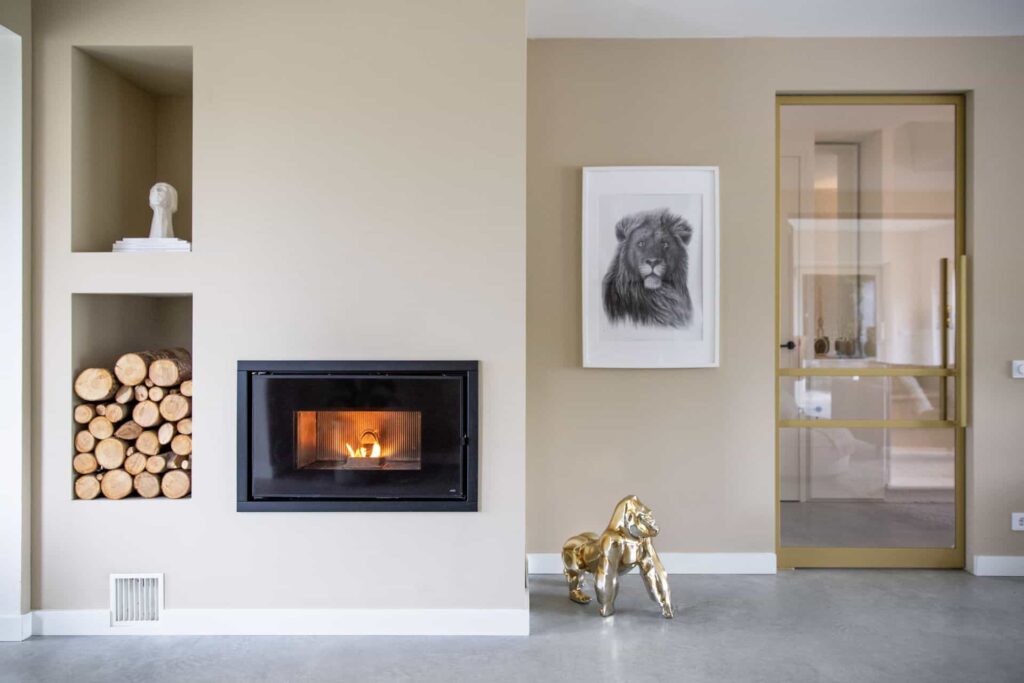 Vrijstaande woning in Brunssum met een beige wand. Hierin zitten nisjes en een open haard. Hiernaast zit een gouden deur en op de gevlinderde betonvloer staat een gouden aap.