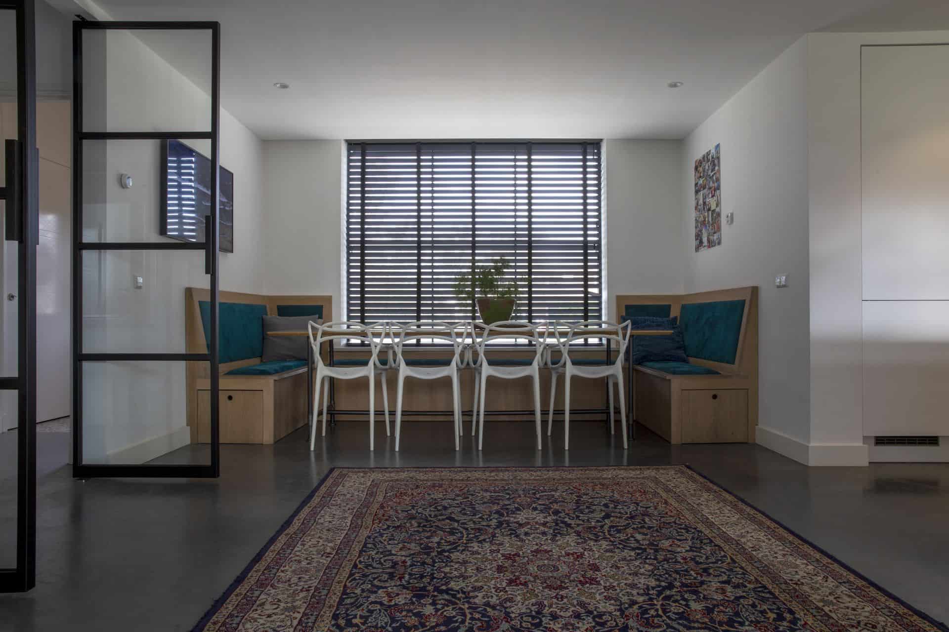 Woning in Beneden-Leeuwen met een gevlinderde betonvloer van Willem Designvloeren in de eetkamer. Dit is gecombineerd met een houten tafel, houten bank en witte stoeltjes. Ook ligt er een gekleurd vloerkleed op de gevlinderde betonvloer.