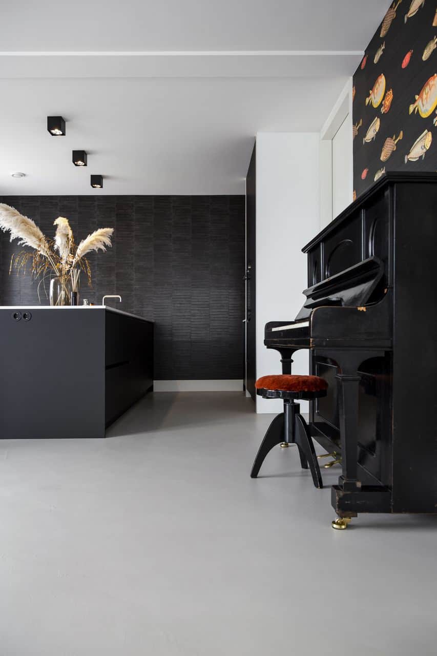 Beton ciré vloer in de keuken gecombineerd met een zwart kookeiland en een zwarte piano.