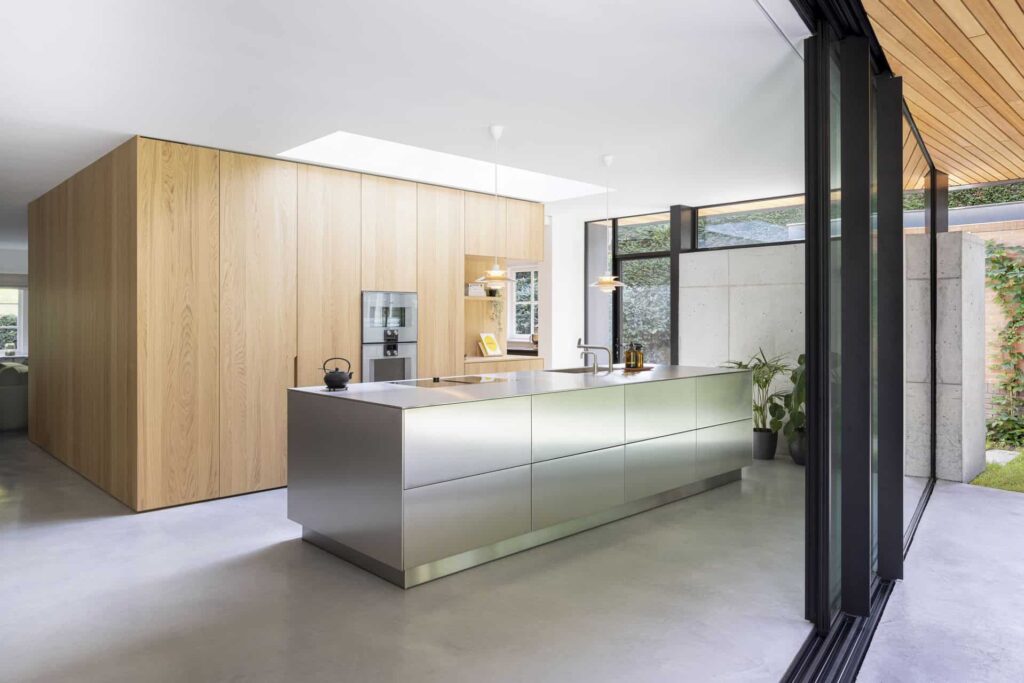 Aanbouw in Zeist met een gevlinderde betonvloer van Willem Designvloeren. Hierop staat een stalen kookeiland en een houten kastenwand.