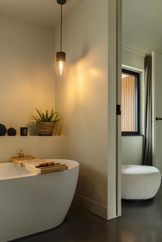 Badkamer in Heemstede met een gevlinderde betonvloer. Op de vloer staat een wit bad met een houten plank.