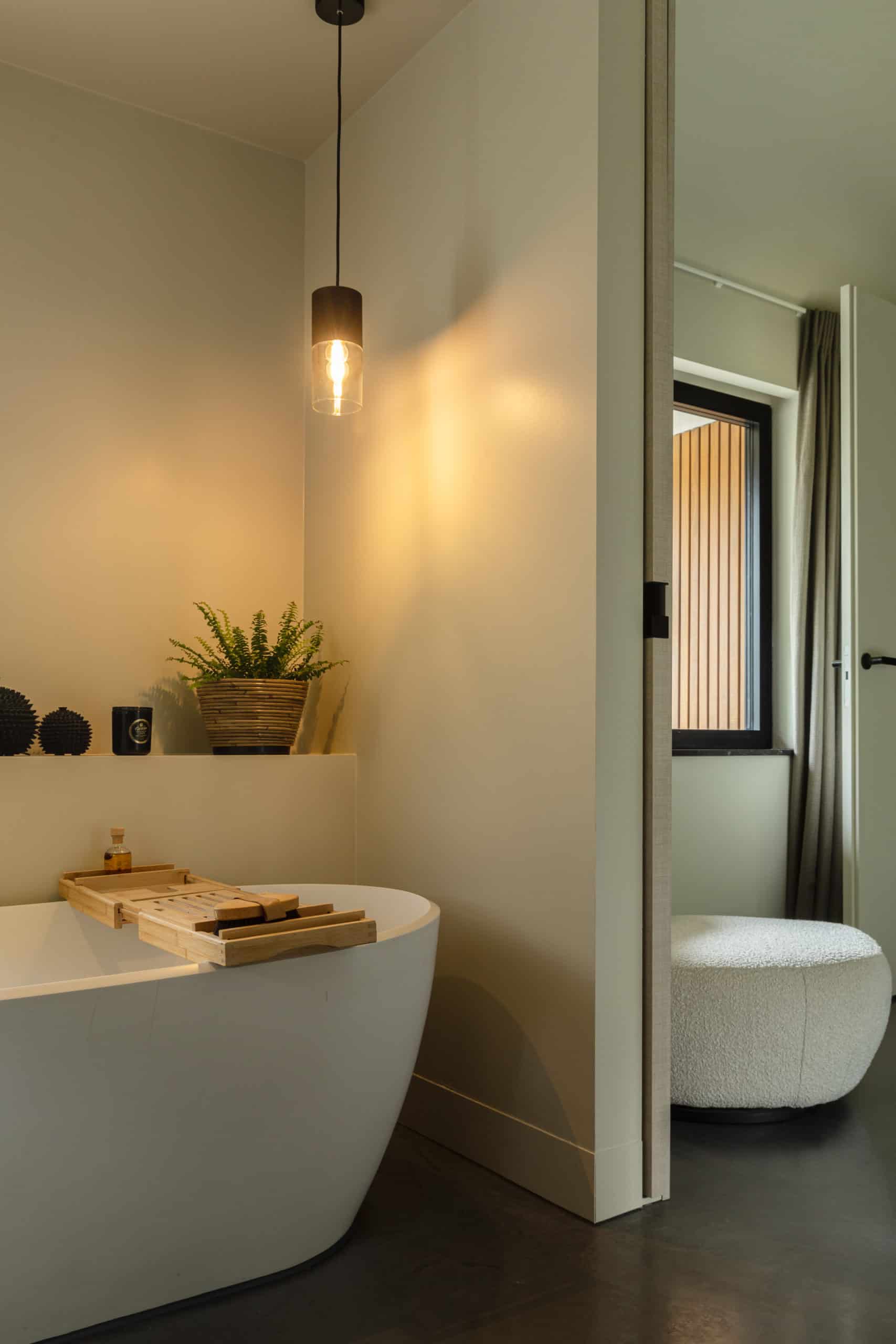 Badkamer in Heemstede met een gevlinderde betonvloer. Op de vloer staat een wit bad met een houten plank.