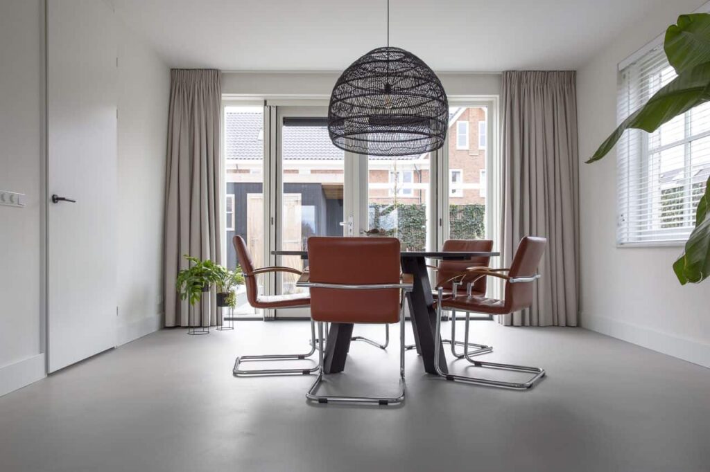 Beton ciré vloer in de eetkamer in Kesteren. Hierop staat een zwarte eettafel met daaraan oranje stoelen.