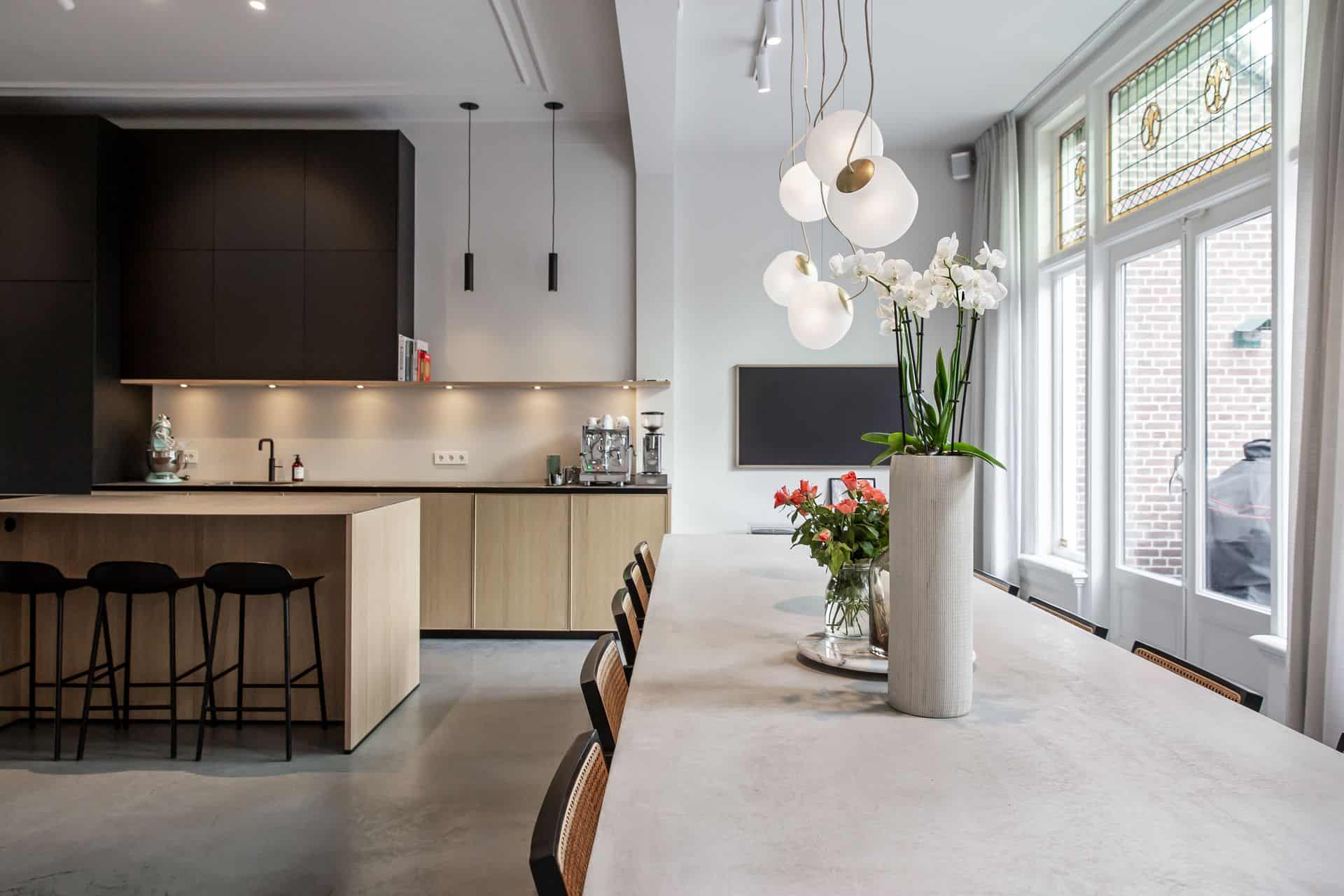 Betonnen tafel met daaraan zwart met rieten stoelen. Op de tafel staan vazen met bloemen.