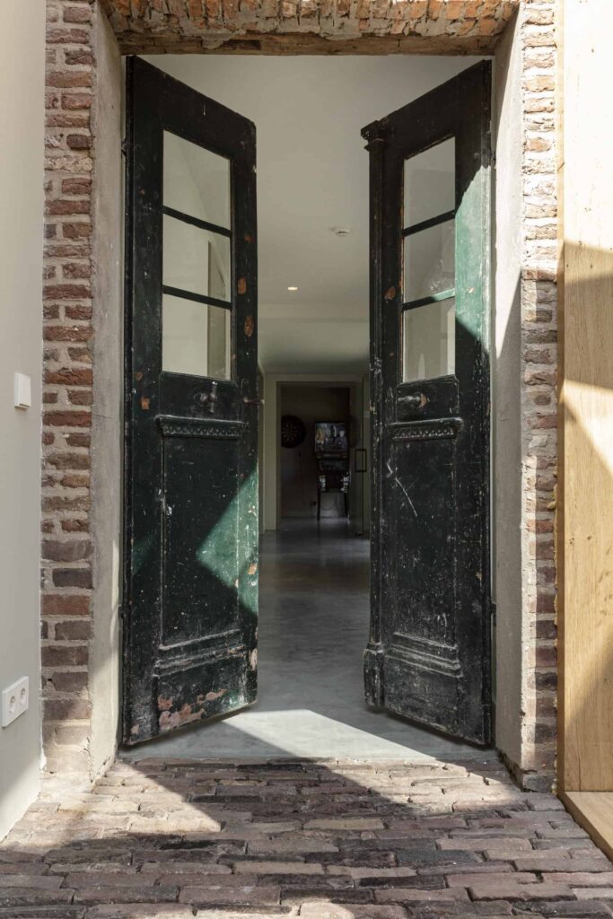 Doorkijkje door twee oude groende deuren naar de hal in Oss waar een gevlinderde betonvloer ligt 1