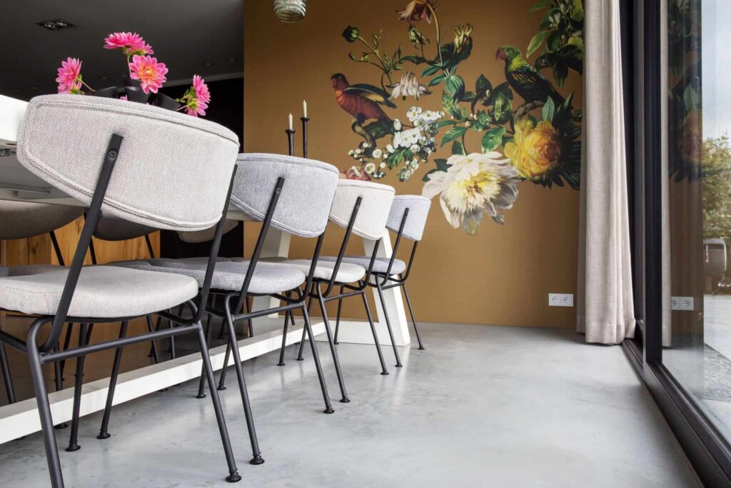 Eetkamer in Kampen met een gevlinderde betonvloer. Hierop staan grijze stoelen met stalen poten. Op de bruine wand zit een muursticker van vogels.