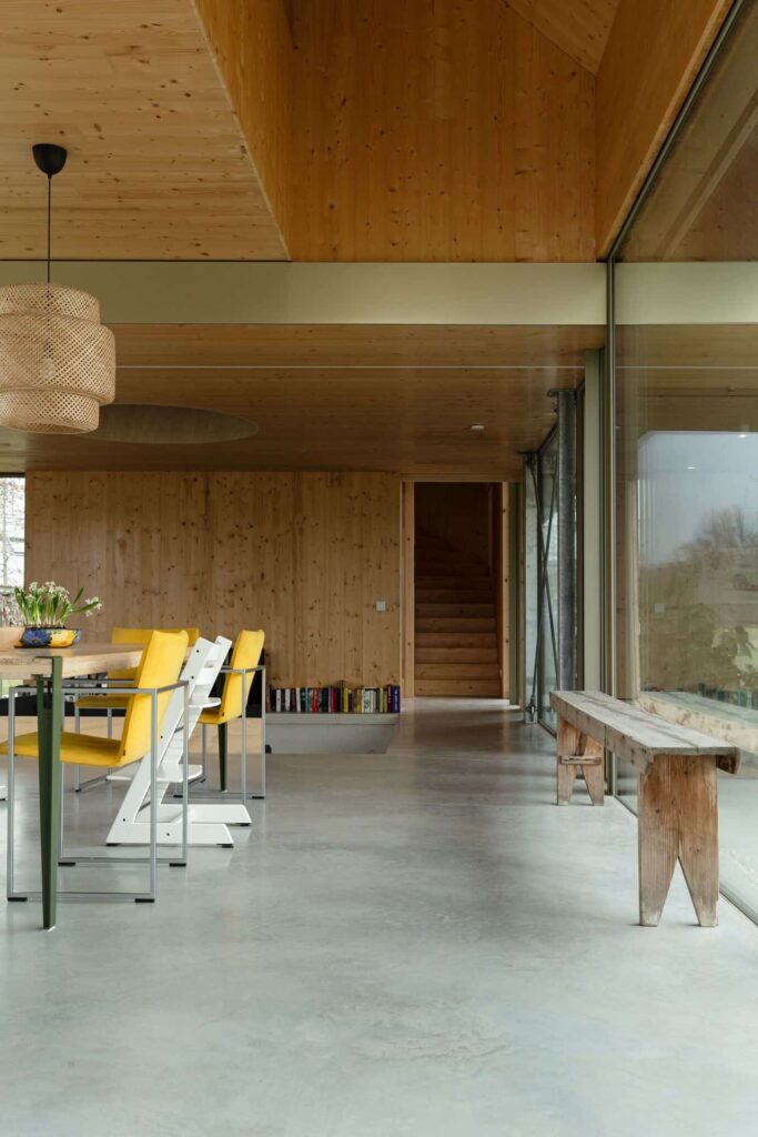 Eetkamer in de Achterhoek met een gevlinderde betonvloer. Hierop staat een houten tafel met gele en witte stoelen.