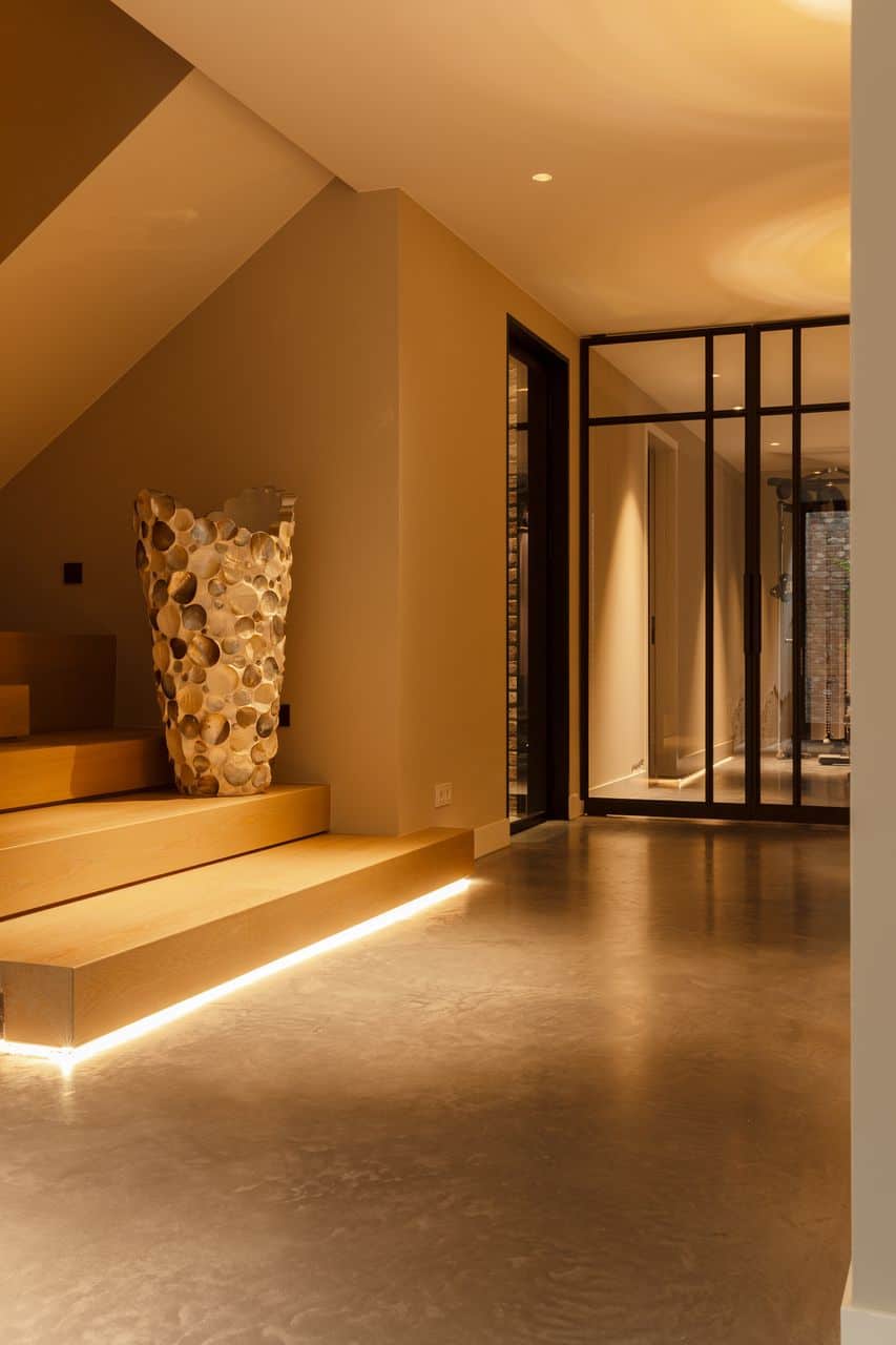 Entree met een gevlinderde betonvloer, gecombineerd met stalen taatsdeuren en een grote houten trap.