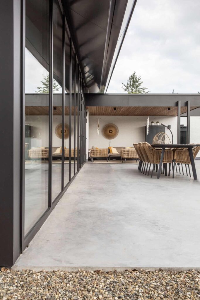 Gevlinderd betonnen terras in Nuenen, hierop staat een zwarte tafel met rieten stoelen.