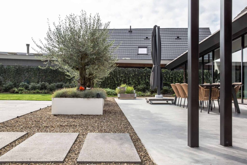 Gevlinderd betonnen terras is Nuenen, gecombineerd met grind, stapstenen en bakken met hierin bomen.