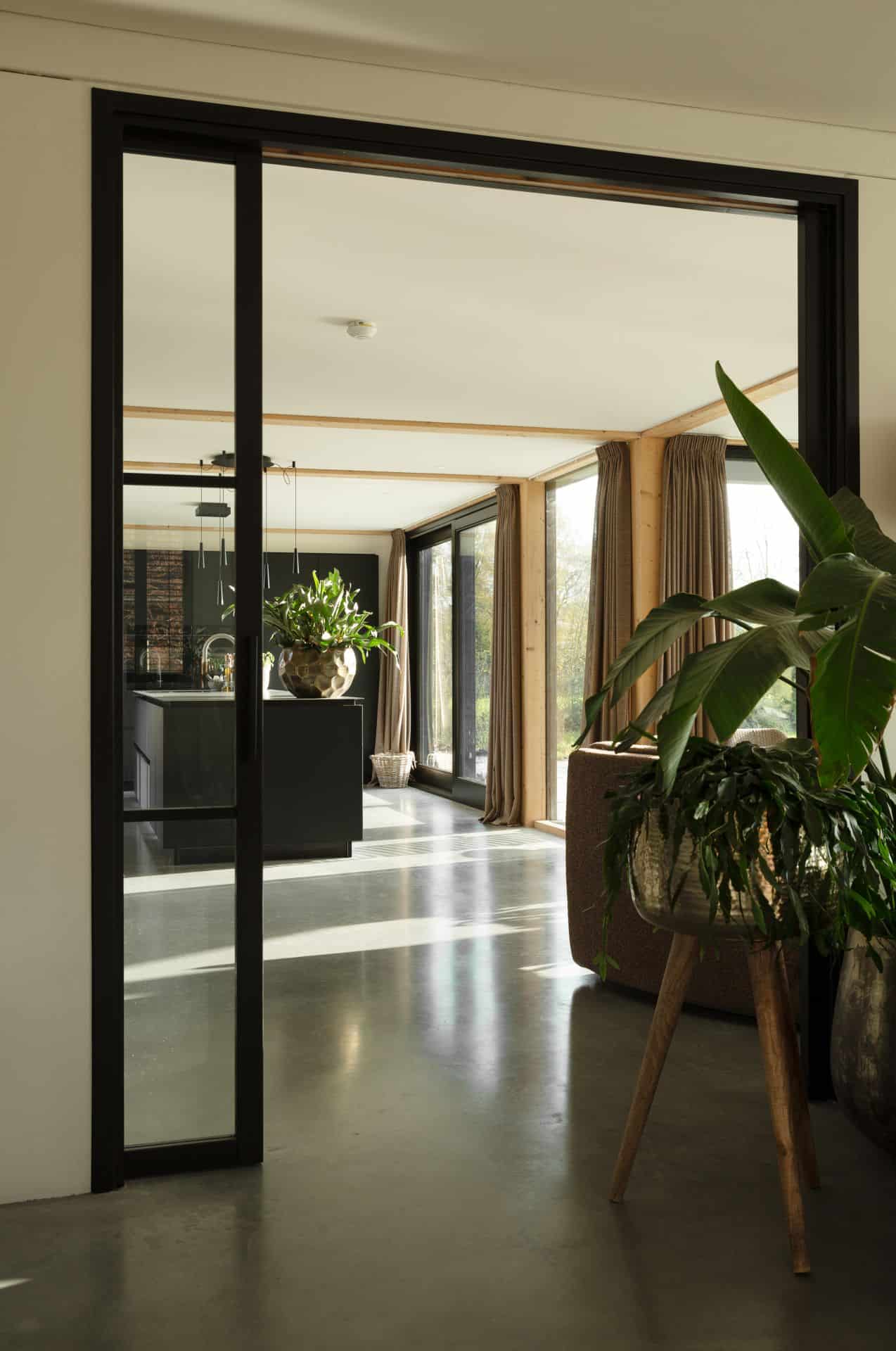 Gevlinderde betonvloer en betonnen terras in Zeist gecombineerd met een zwart kookeiland en zwarte stalen deuren.