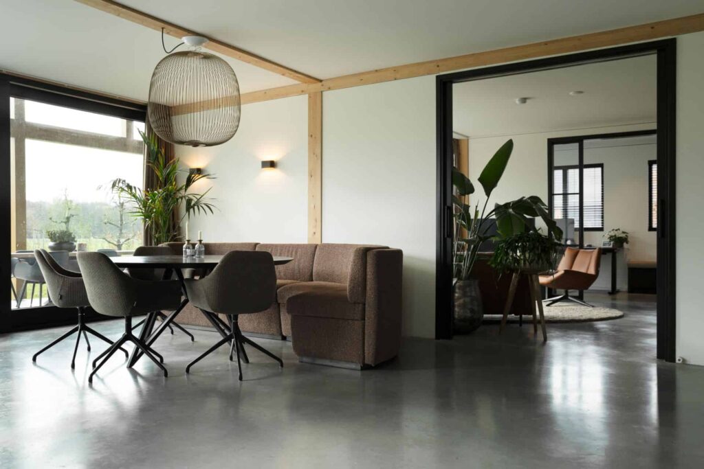 Gevlinderde betonvloer en betonnen terras in Zeist hierop staat een zwarte eettafel met daaraan een bruine bank en grijze stoelen.