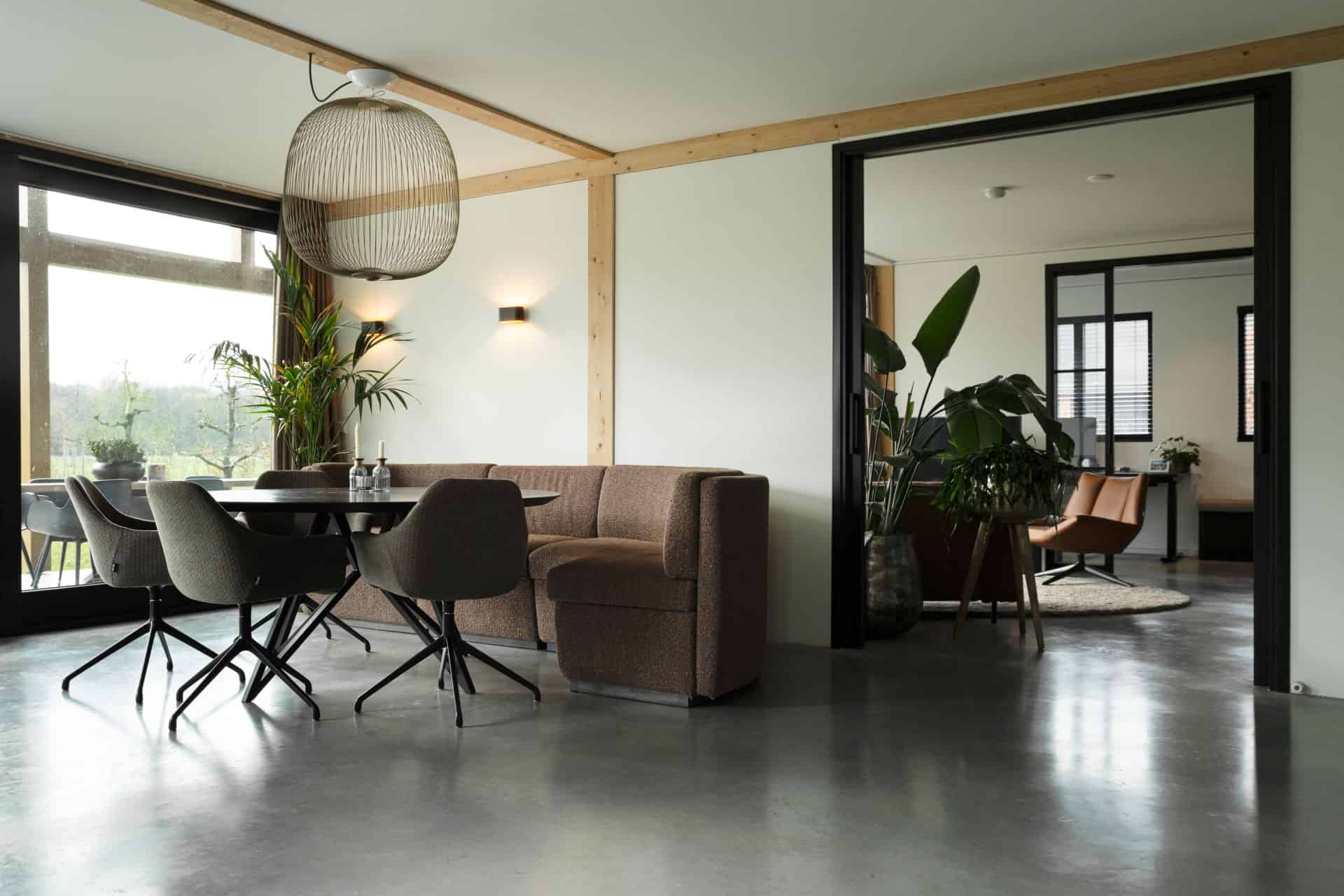 Gevlinderde betonvloer en betonnen terras in Zeist hierop staat een zwarte eettafel met daaraan een bruine bank en grijze stoelen.