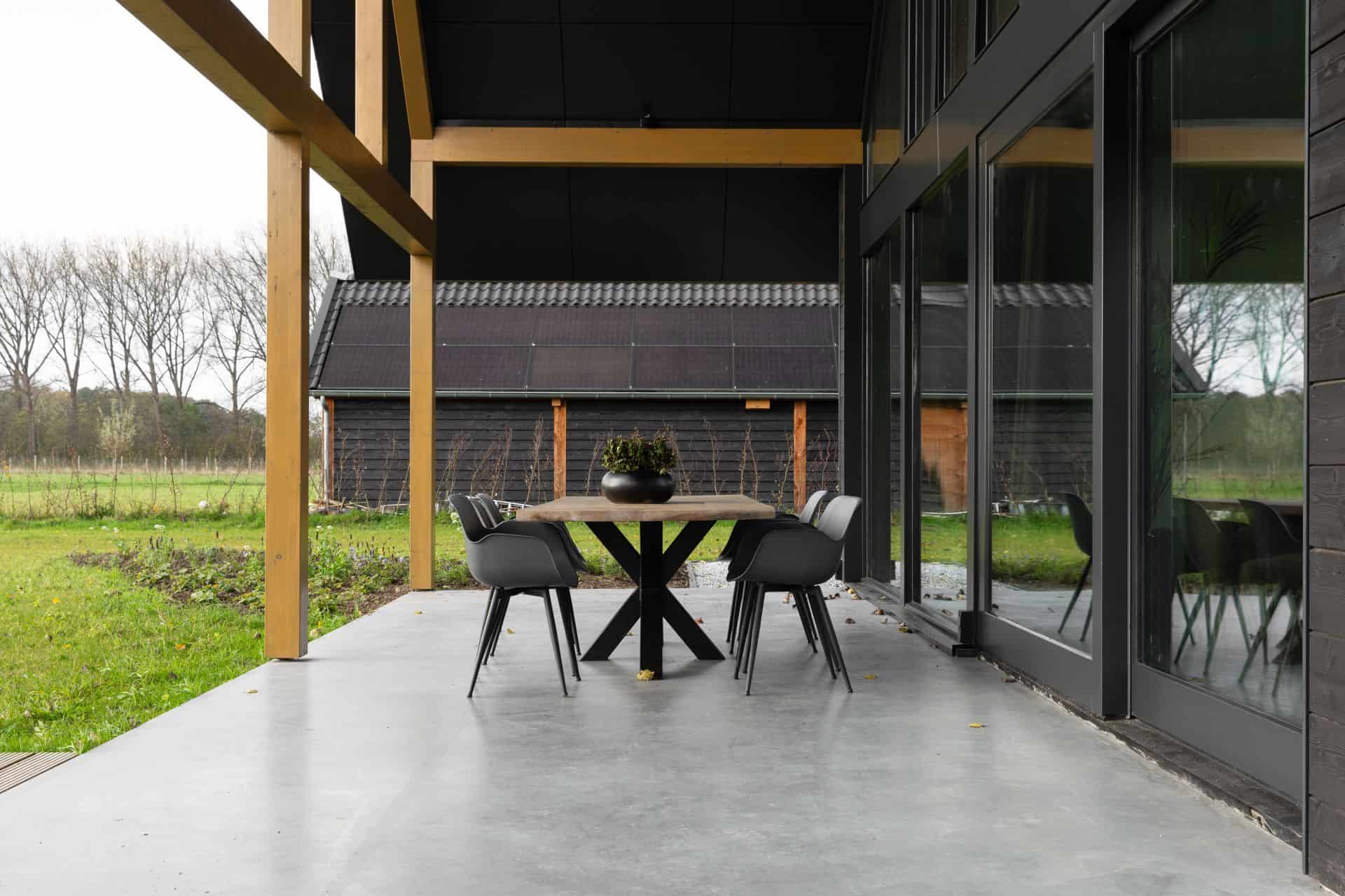 Gevlinderde betonvloer en betonnen terras in Zeist. Op het terras staat een houten tafel met zwarte poten en daaraan zwarte stoelen.