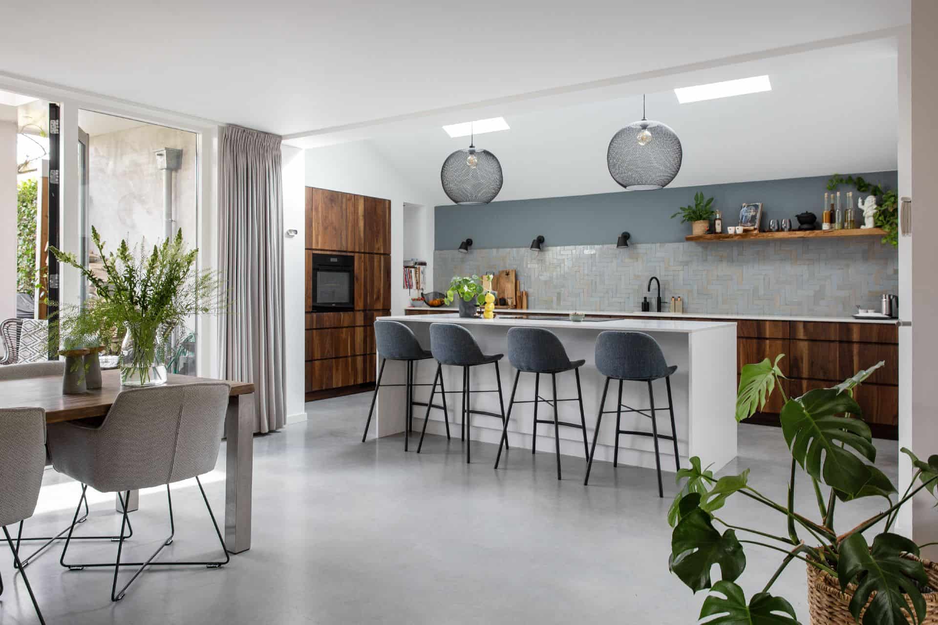 Gevlinderde betonvloer in Brede met daarop een wit kookeiland en een houten keuken. Aan het kookeiland staat 4 barkrukken.