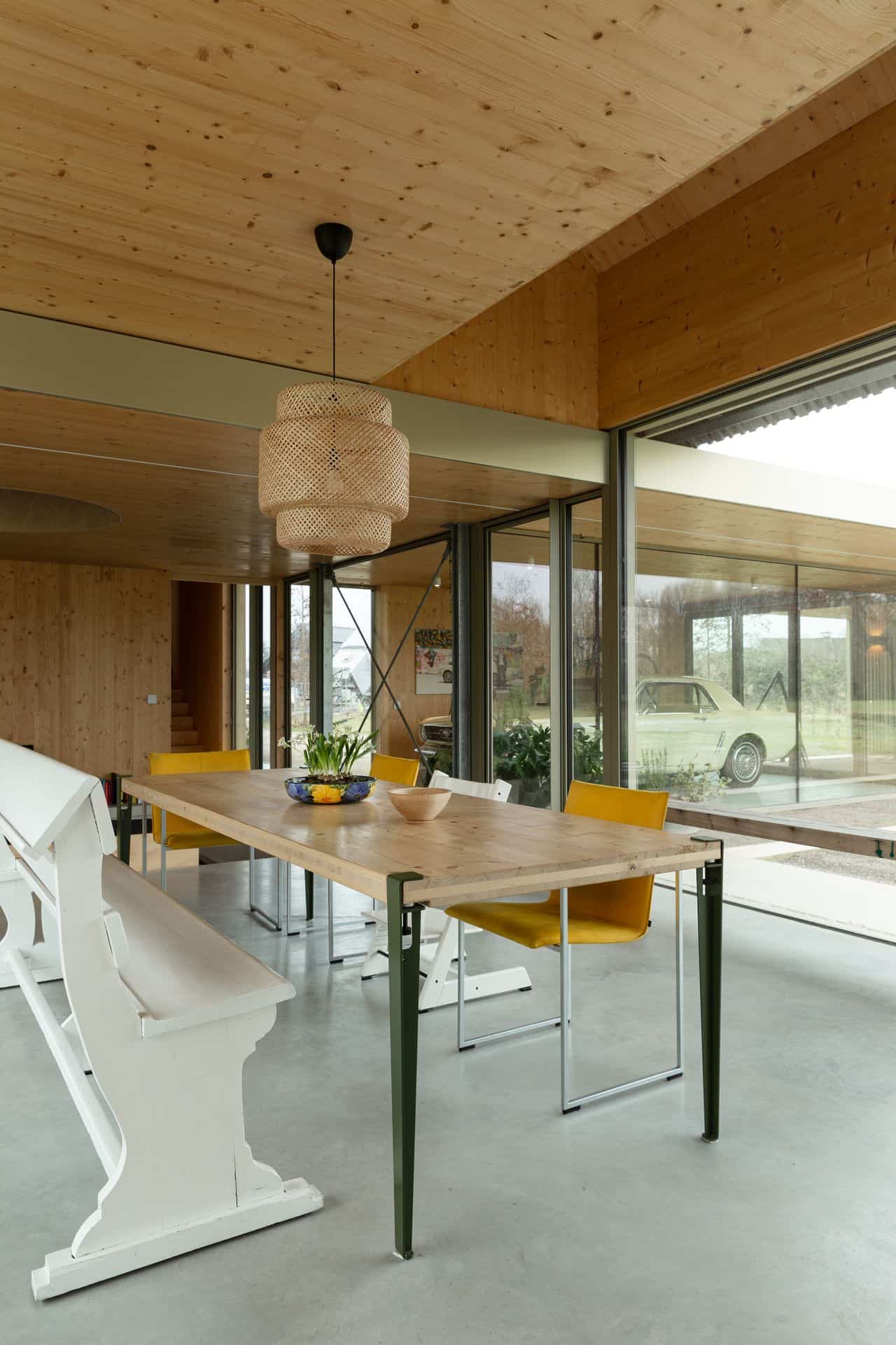 Gevlinderde betonvloer in de Achterhoek met daarop een houten tafel met een witte kerkbank en witte en gele stoelen.