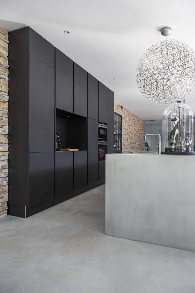 Gevlinderde betonvloer in de keuken in Nijmegen. Hierop staat een zwarte keuken en een RVS kookeiland.