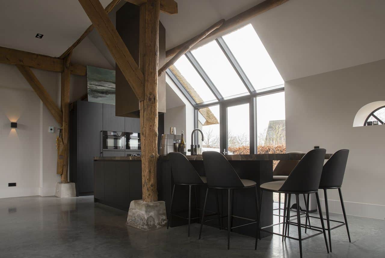 Gevlinderde betonvloer in de keuken in Ochten. De keuken is zwart met een marmeren blad. Aan het kookeiland staat zwarte barkrukken.