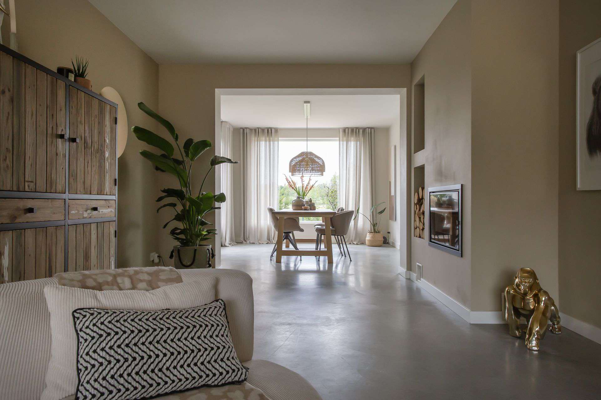 Gevlinderde betonvloer in een vrijstaande woning in Brunssum. Hierop staat een beige stoel, houten tafel met daaraan beige stoelen en een gouden aap.