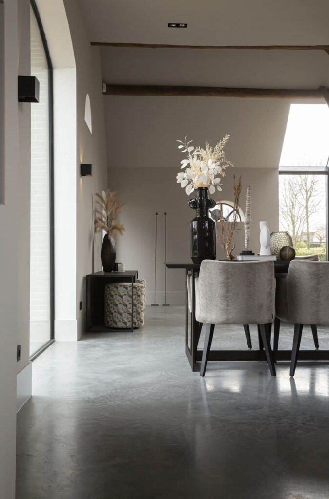 Gevlinderde betonvloer in een woning in Ochten gecombineerd in een landelijk interieur met een zwarte eettafel en daaraan grijze stoelen.
