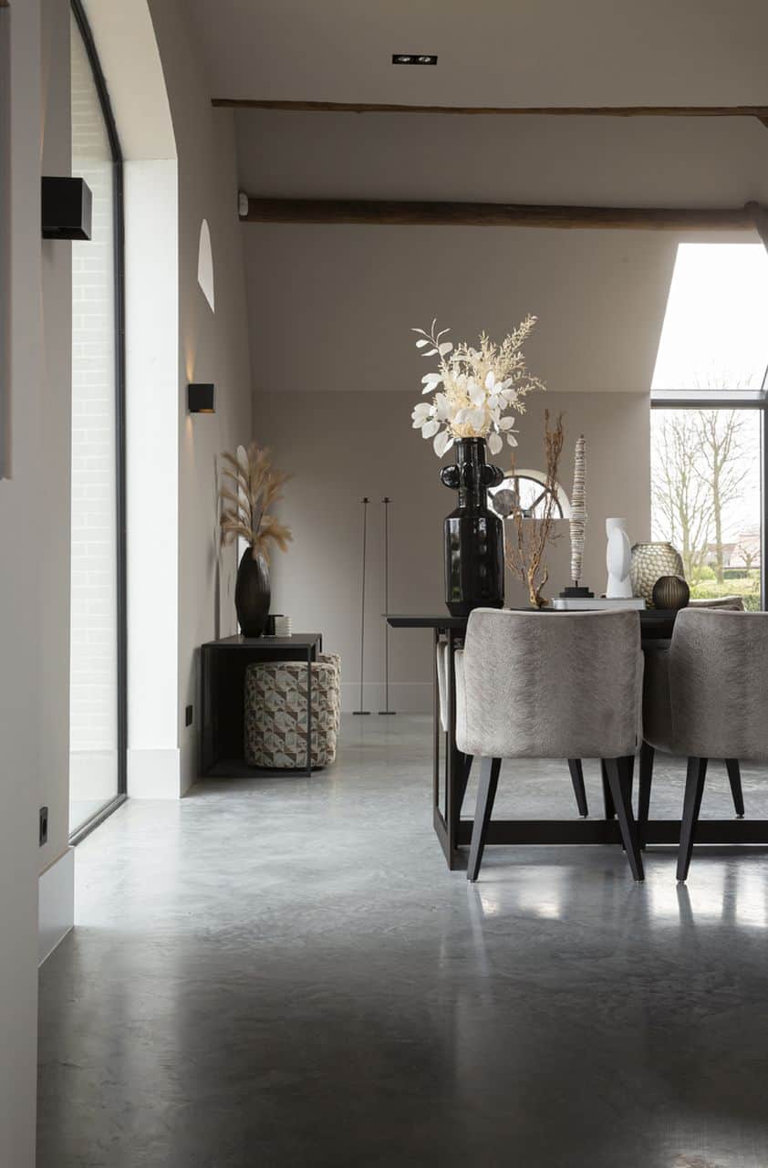 Gevlinderde betonvloer in een woning in Ochten gecombineerd in een landelijk interieur met een zwarte eettafel en daaraan grijze stoelen.