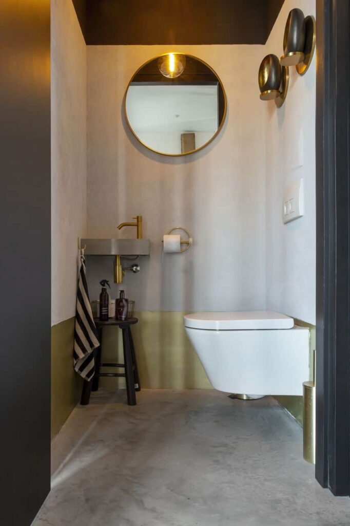 Gevlinderde betonvloer in het toilet in Schoonhoven gecombineerd met een wit toilet. Op de onderkant van de wand zit een gouden rand.