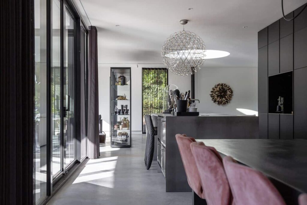 Gevlinderde betonvloer van Willem Designvloeren met daarop een RVS keuken en daaraan zwarte barkrukken.