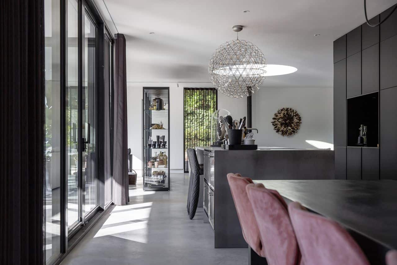 Gevlinderde betonvloer van Willem Designvloeren met daarop een RVS keuken en daaraan zwarte barkrukken.