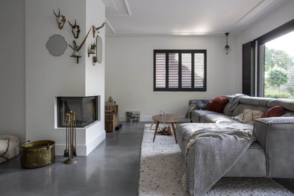 Gevlinderde woonbeton vloer in de woonkamer in Tilburg met daarop een wit vloerkleed en een grijze bank.