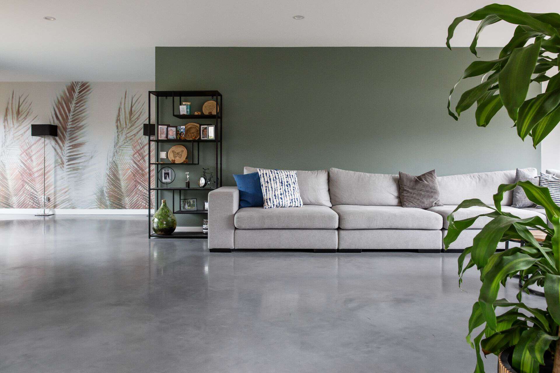 Grijze bank op een gevlinderde betonvloer in Strijen. Naast de bank staat een zwart stalen kast met daaraan foto's en accessoires.