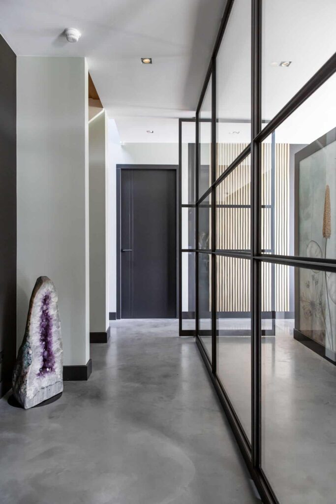 Hal in Nuenen met een gevlinderde betonvloer. In de hal zit een glazen wand met stalen omranding. In de hal staat een halve kristal.