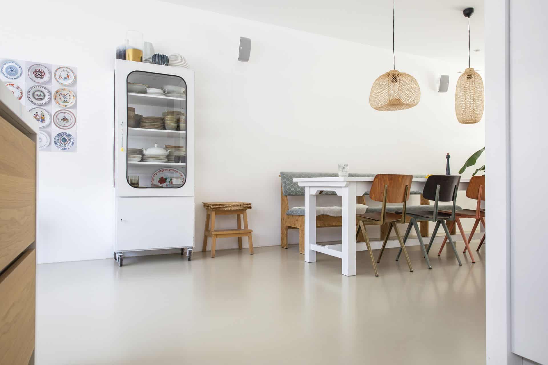 PU gietvloer van Willem Designvloeren in Zeist. Hierop staat een witte eettafel met daaraan houten stoelen en een houten bank.