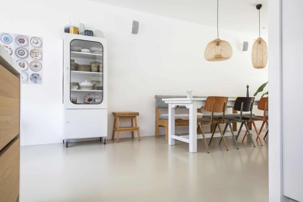 PU gietvloer van Willem Designvloeren in Zeist. Hierop staat een witte eettafel met daaraan houten stoelen en een houten bank.