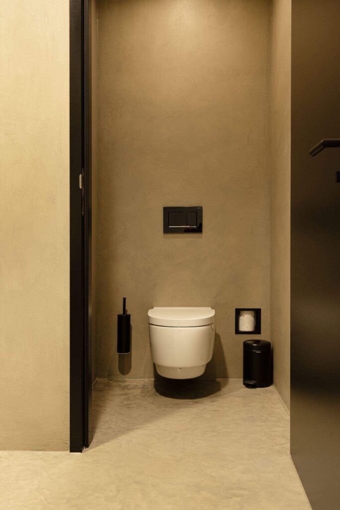 Toilet met beton ciré wanden en een gevlinderde betonvloer in een kantoorpand in Hattemerbroek.