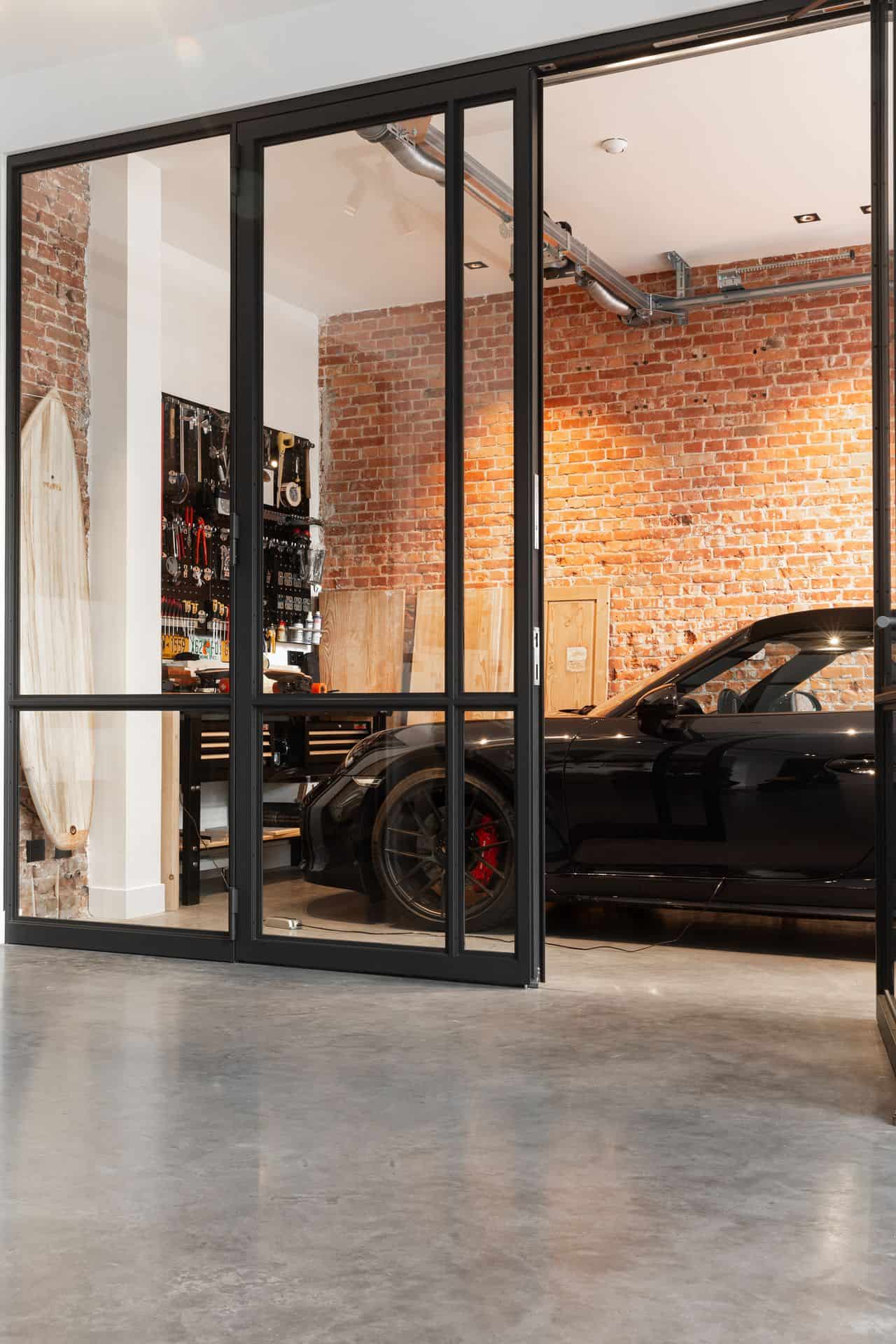 Woning in Den Haag met een gevlinderde betonvloer. Op de betonvloer staat een Porsche achter zwarte stalen deuren.