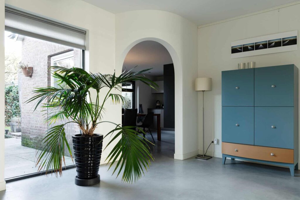 Woning in Rosmalen. Hierin ligt een gevlinderde betonvloer. Op de betonvloer staat een plant in een zwarte pot. Je kijkt door naar de keuken. Deze zit achter een ronde doorgang.