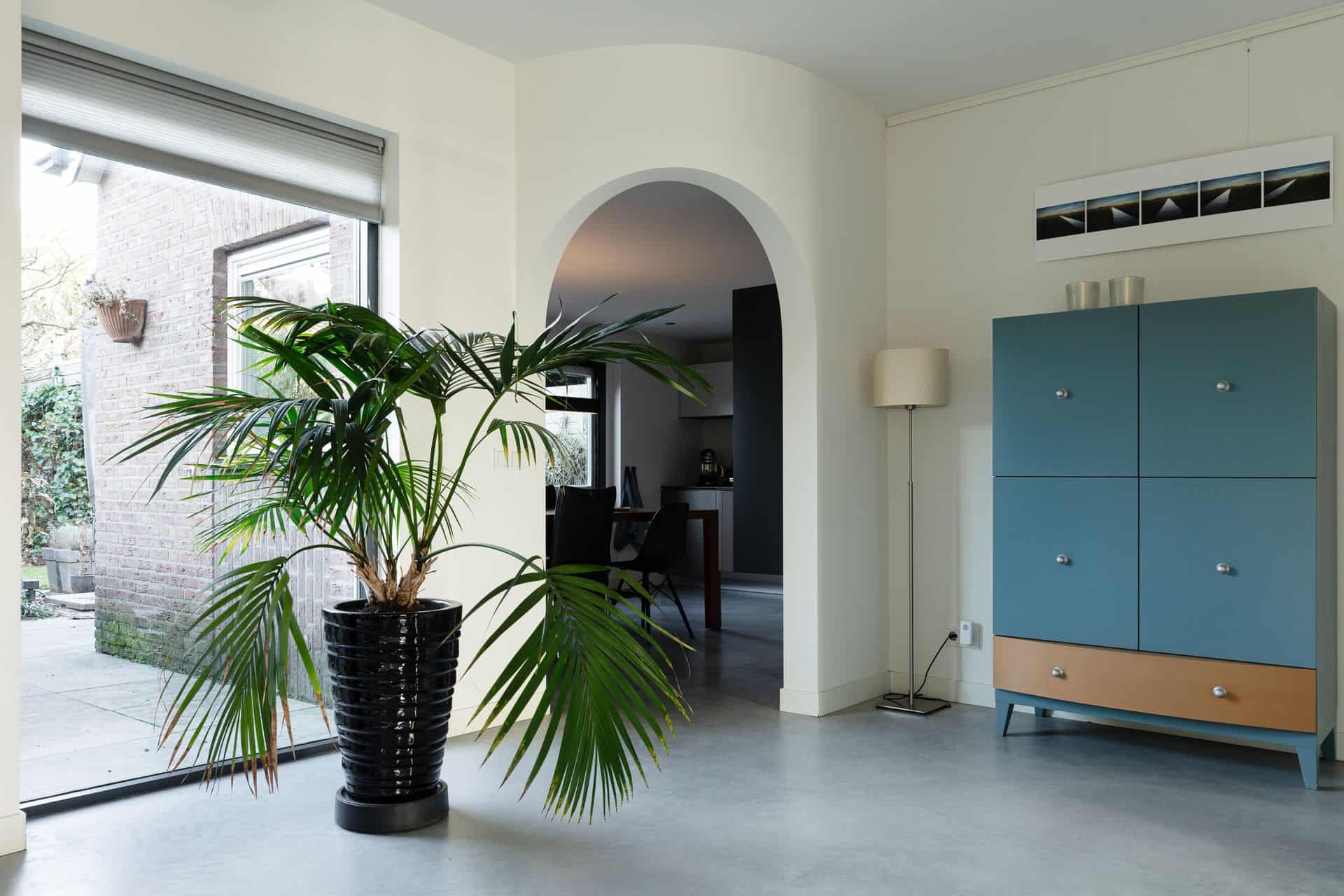 Woning in Rosmalen. Hierin ligt een gevlinderde betonvloer. Op de betonvloer staat een plant in een zwarte pot. Je kijkt door naar de keuken. Deze zit achter een ronde doorgang.