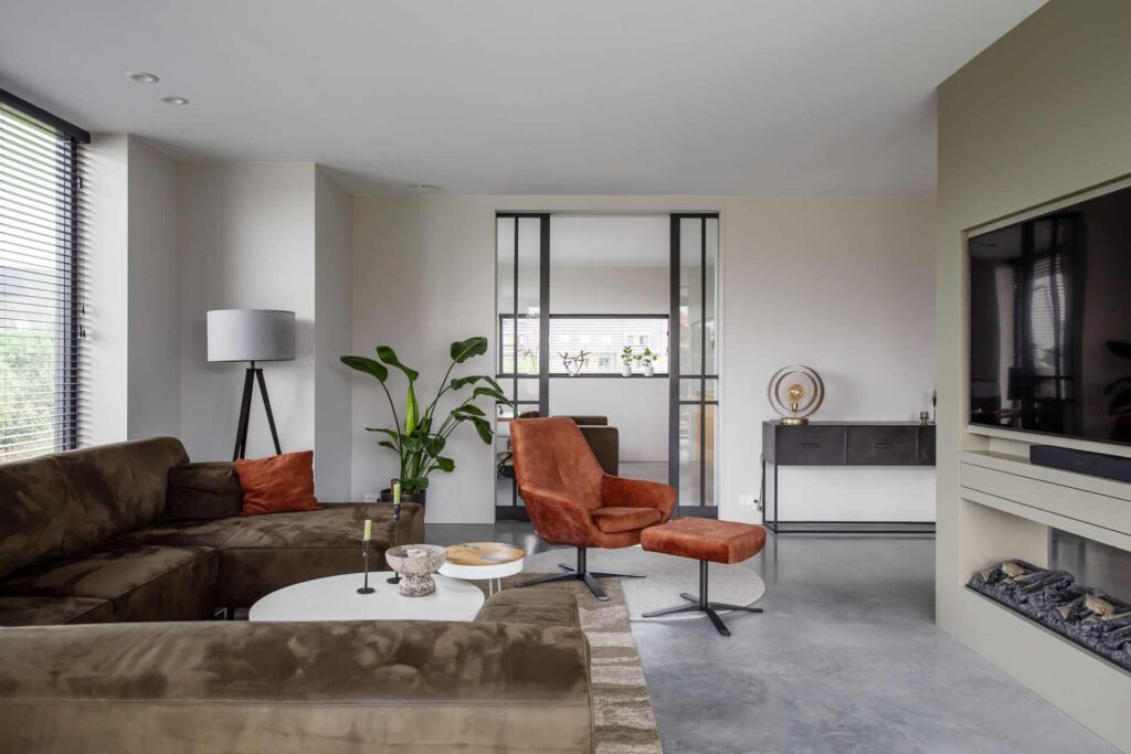 Woonkamer in Kampen met een gevlinderde betonvloer. Hierop staat een bruine bank en oranje stoelen.