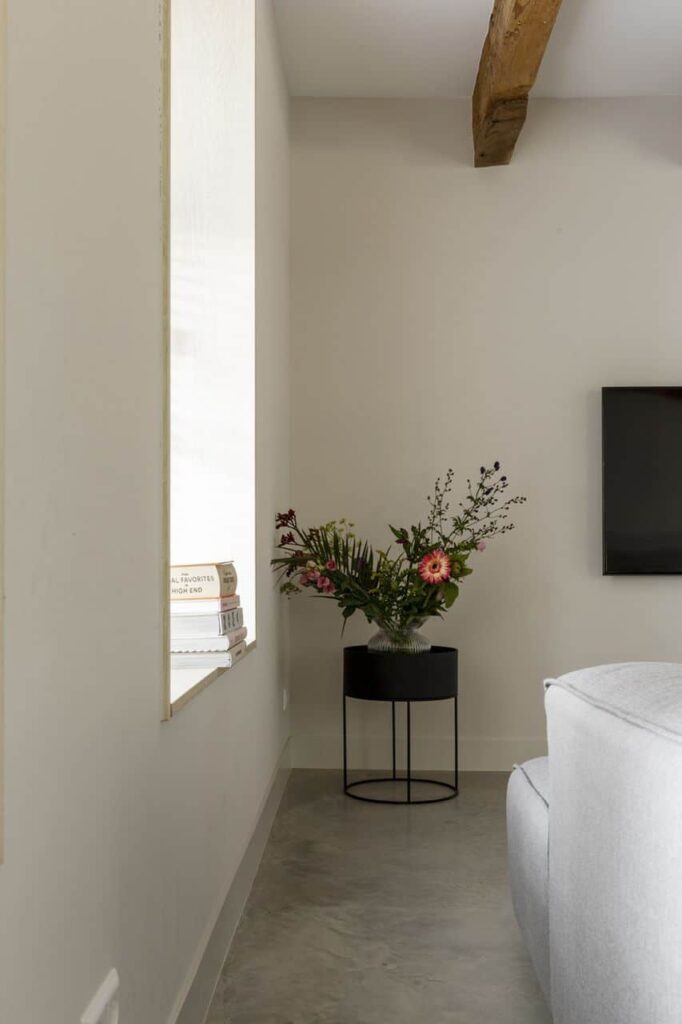 Woonkamer in Kloetinge met een gevlinderde betonvloer van Willem Designvloeren, gecombineerd met een grijze bank en een zwart tafeltje met daarop bloemen.