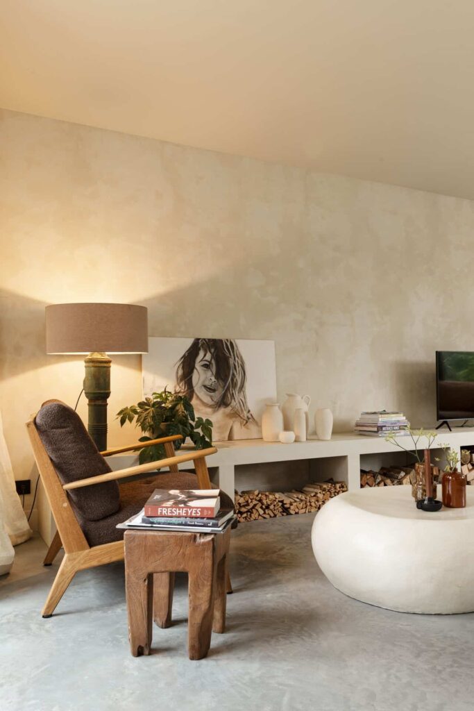 Woonkamer in Rijnsburg. Hierin ligt een gevlinderde betonvloer. Hierop staat een houten stoel en bijzettafel. De wanden zijn in een zandkleur.