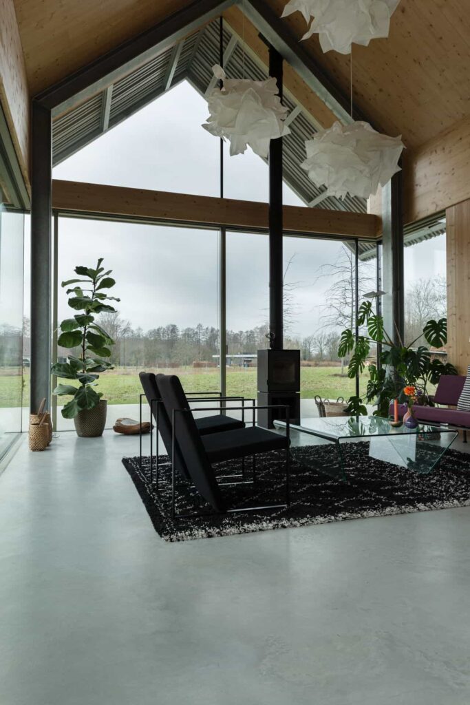 Woonkamer in de Achterhoek met een gevlinderde betonvloer. Hierop ligt een zwart vloerkleed met zwarte stoelen en een paarse bank.