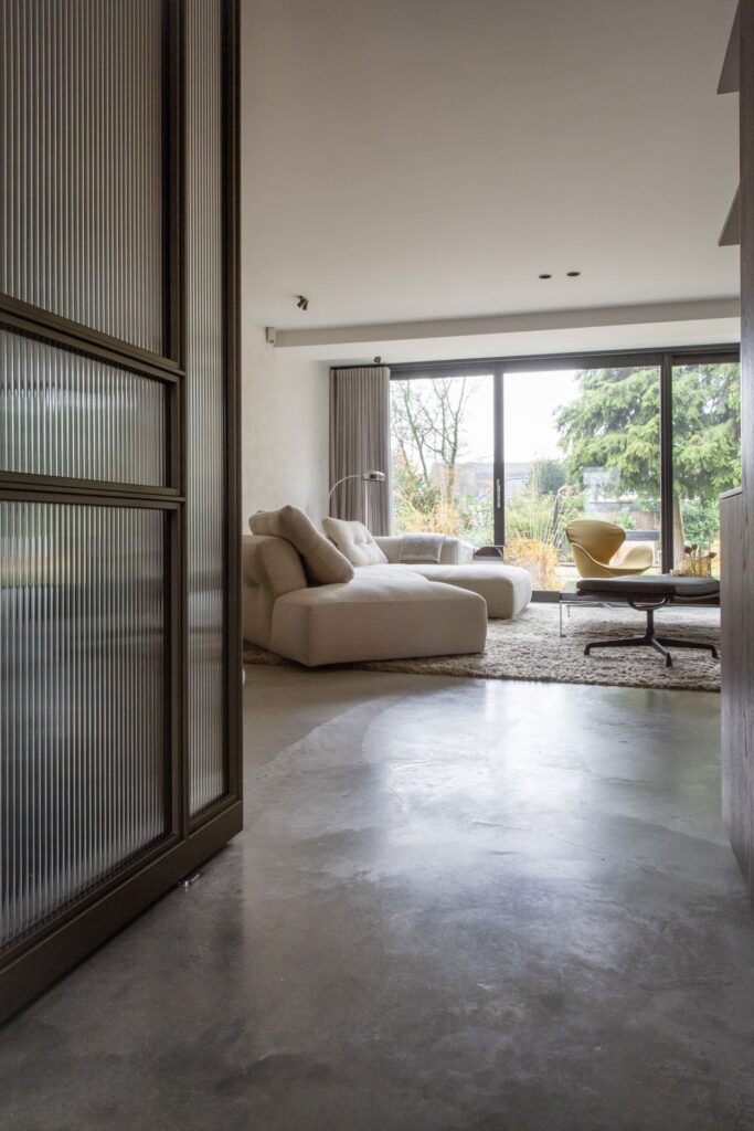 Woonkamer met een beige bank in Waalwijk. Deze staat op een vloerkleed, op een gevlinderde betonvloer.