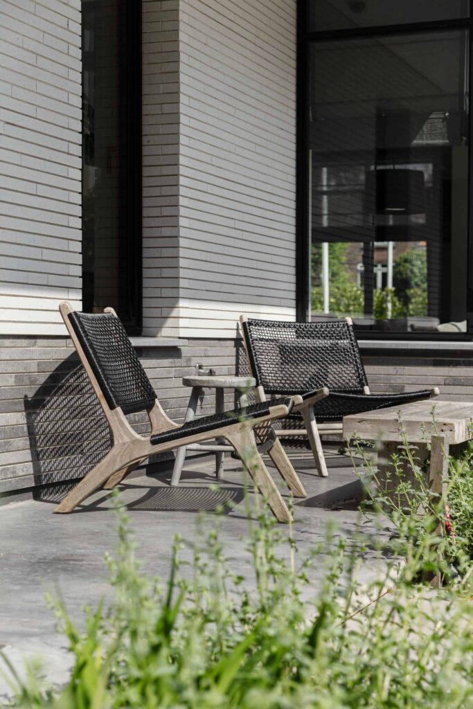 Zithoekje op het gevlinderde betonnen terras in Heemstede. Hier staan 2 houten stoelen en een houten tafeltje