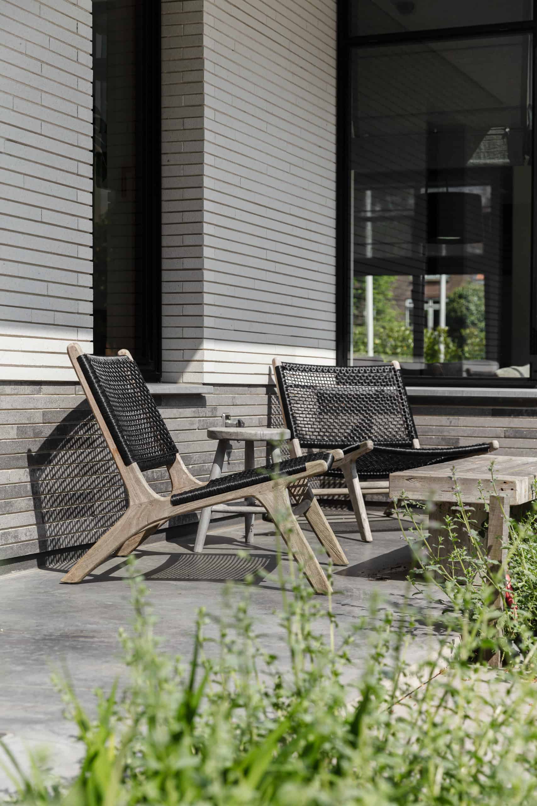 Zithoekje op het gevlinderde betonnen terras in Heemstede. Hier staan 2 houten stoelen en een houten tafeltje