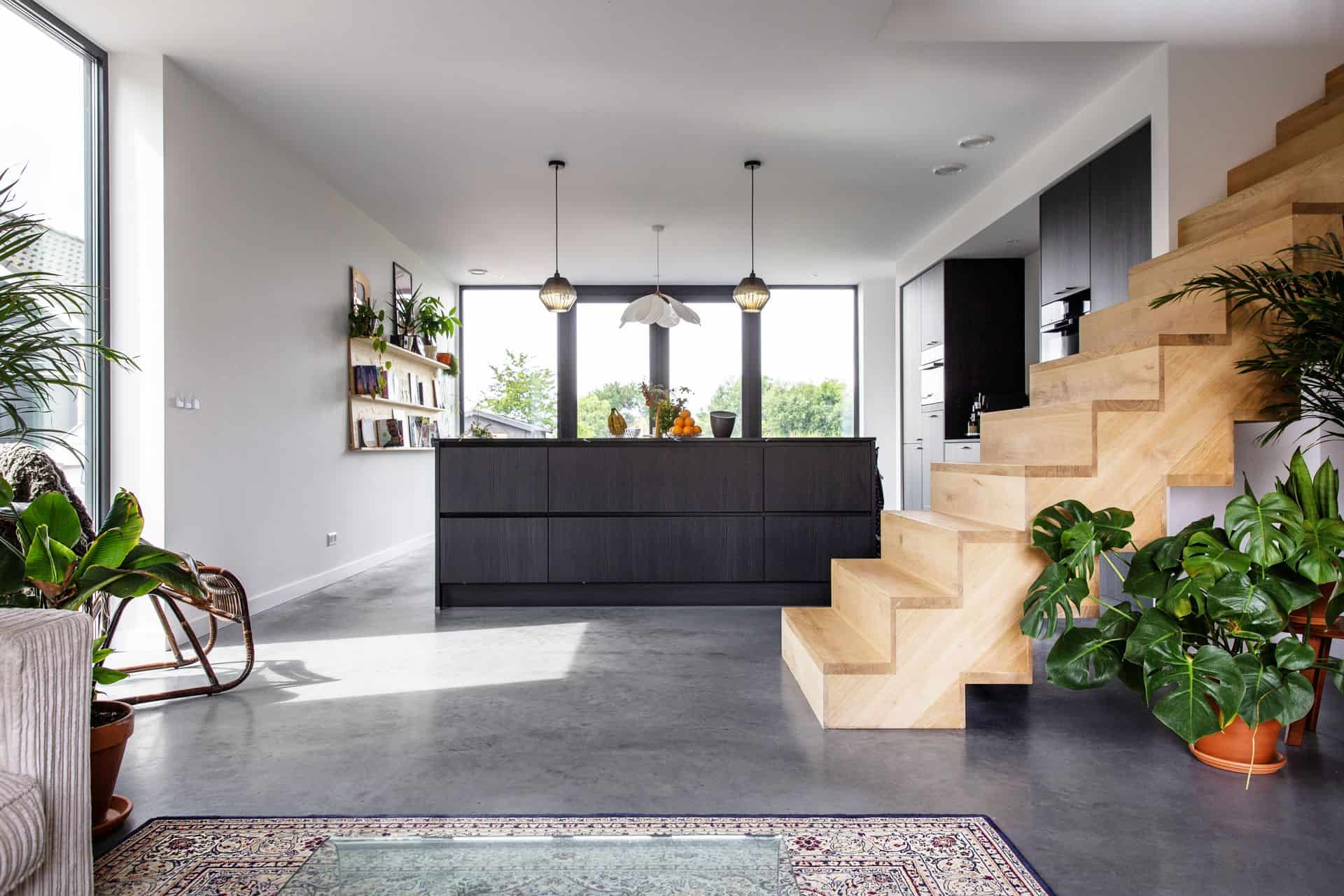 Zwarte keuken in Zijdewind met daarvoor een houten trap. Dit is gecombineerd met een gevlinderde betonvloer