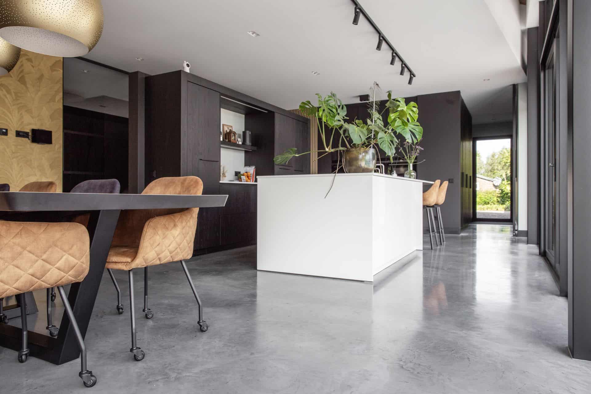 Zwarte keuken met een wit kookeiland in Nuenen, gecombineerd met een gevlinderde betonvloer.